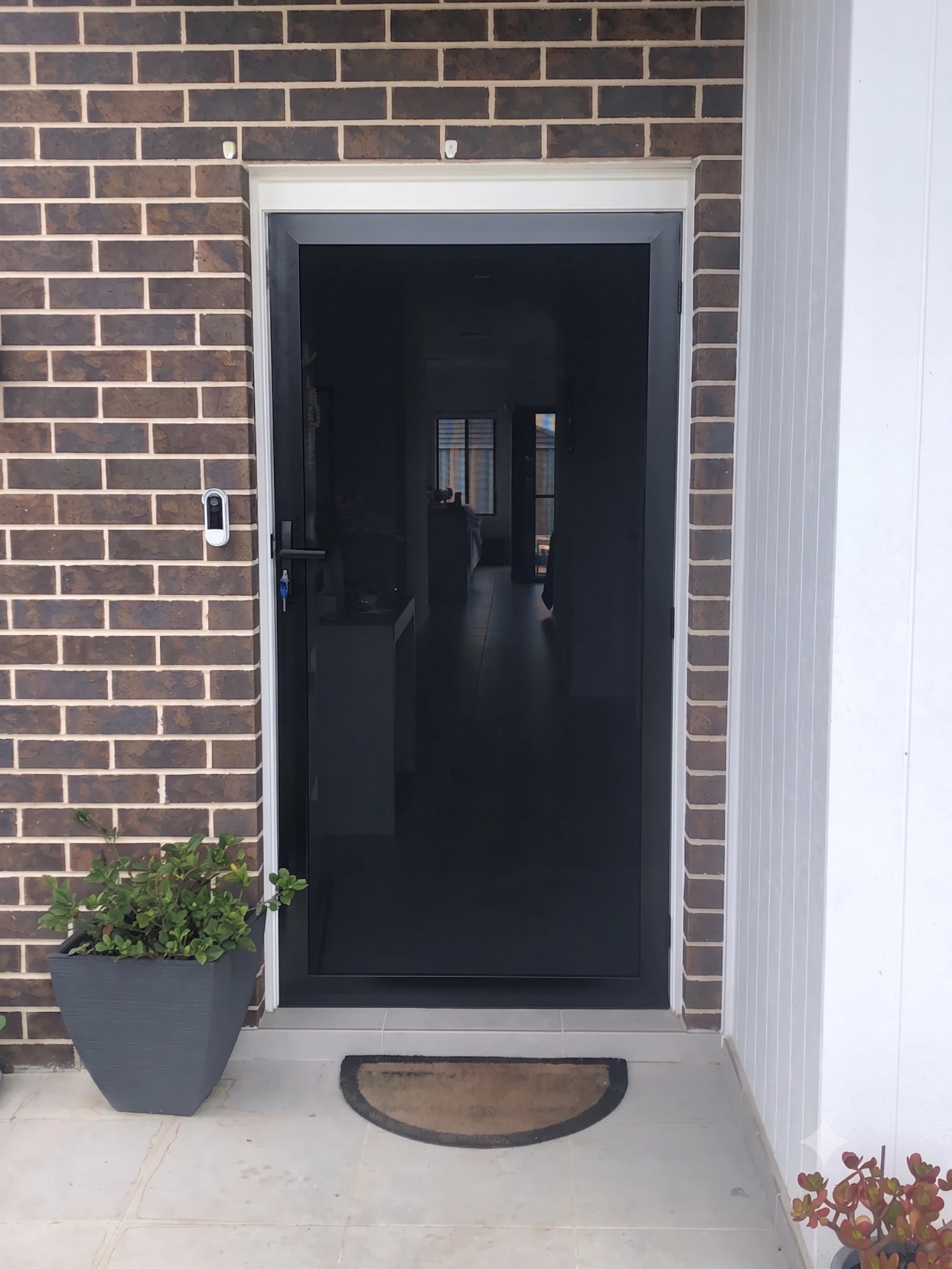 Black hinged security screen door installed on a brick-front Gold Coast home by Gold Coast Blinds and Shutters